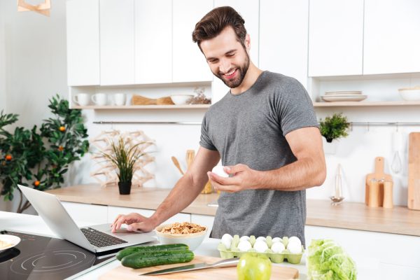 Man with laptop preparing food at the kitchen at home